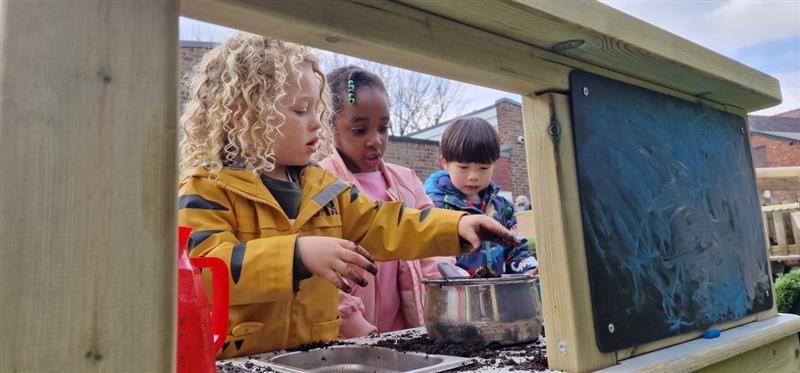 three children play cafe on the essentials mud kitchen