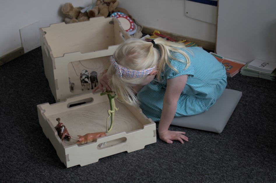 A little girl is playing with toy farm animals and is using the wooden Stack and Sit stool as a prop.