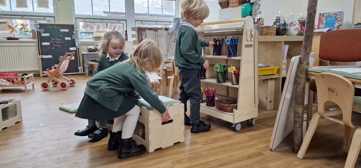 Three children are looking through the indoor classroom furniture as they look for resources to play with and engage with.