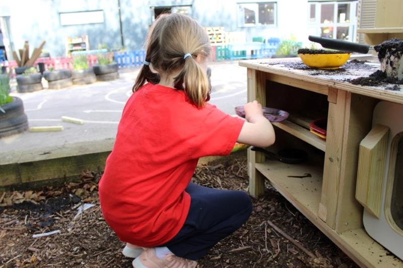 a child kneels and reaches into the mud kitchen for more resources 