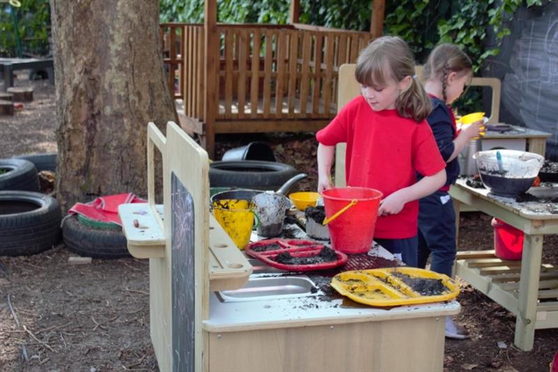 children stand at the mud kitchen and pretend to cook