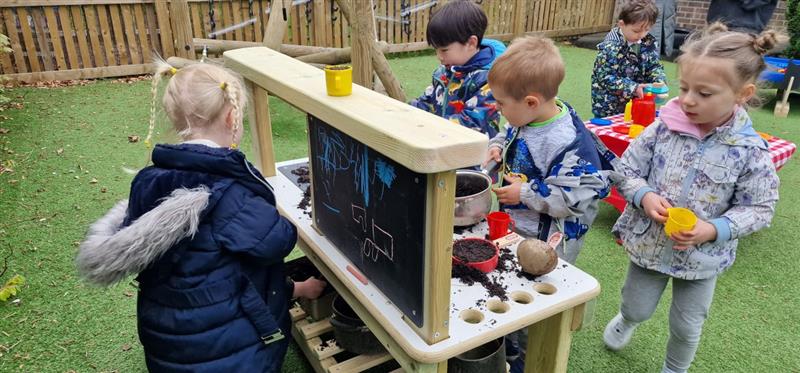 children stand around the mud kitchen and play together