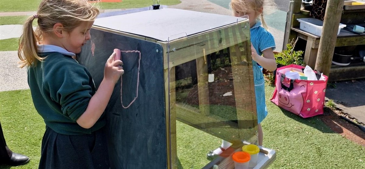 A little girl in primary school is drawing on the freestanding group art easel, as another girl draws on the other side.