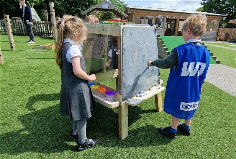 children stand around the group art easel and use paint and chalk to draw on the surfacing 