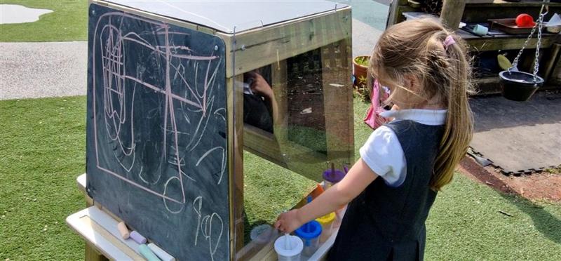 a little girl stands at the paint panel of the group art easel and thinks about what to paint