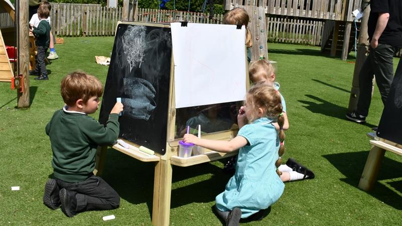 children kneel on the floor in front of the art easel and draw on the paper and the chalkboard sides