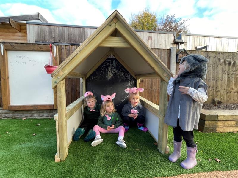 three children sit in the essentials play house and a little girl pretends to be a wolf outside