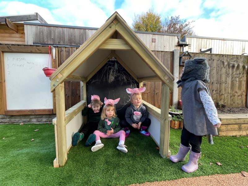 three children dressed as little pigs sit in the playhouse 