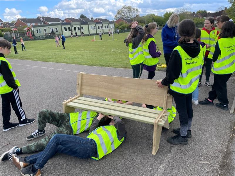 children sit under the bench and look up as they lock the pieces in place