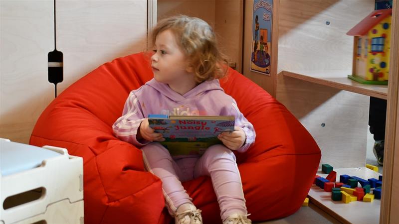 a little girl sits in a red beanbag and reads a storybook