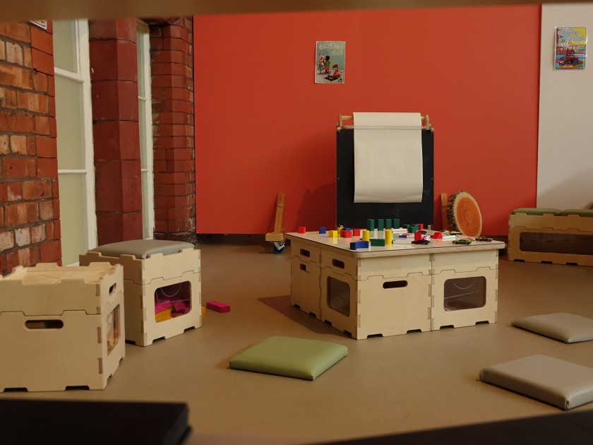 An empty classroom with Pentagon Play's furniture on display. There is a table, a selection of chairs and a variety of toys on the table.