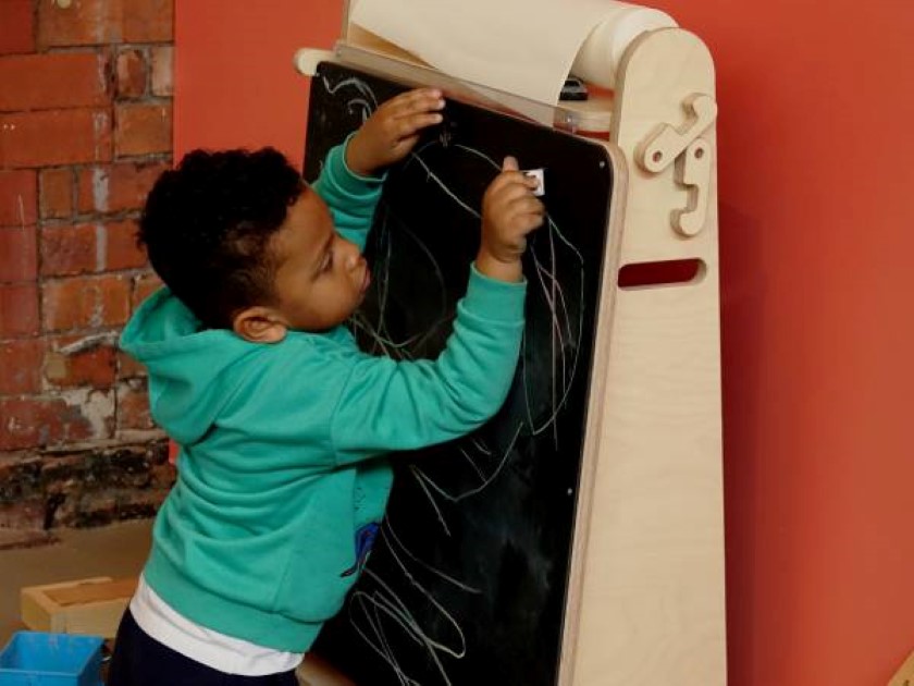 A little child is drawing on a chalkboard with a white piece of chalk. The child is very close to the board.