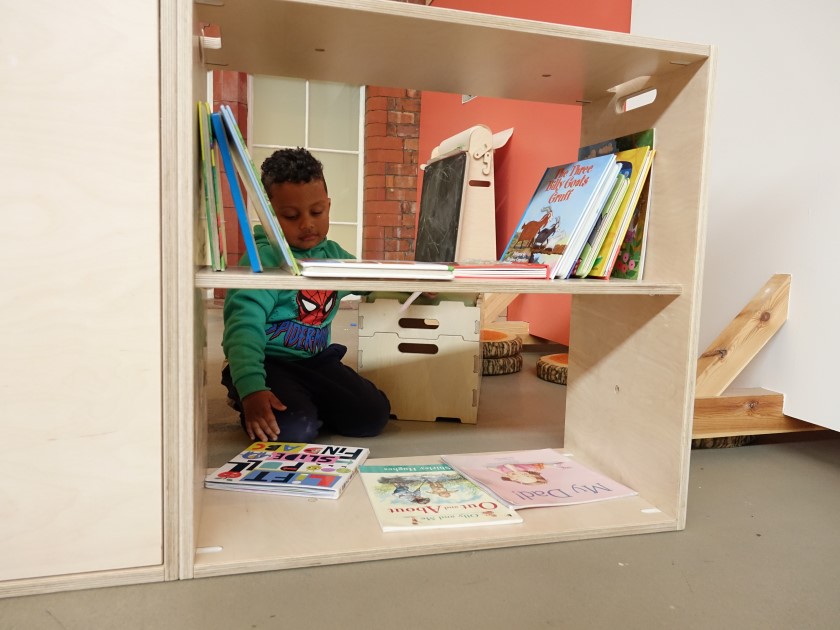 A child is looking through a bookshelf and is selecting a book from it. The child is looking on the bottom shelf.