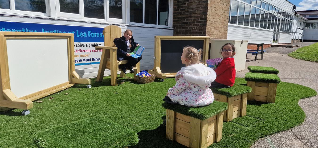 A little girl is sat on a Freestanding Storytelling chair, as her two friends are sat opposite on artificial grass topped seats.