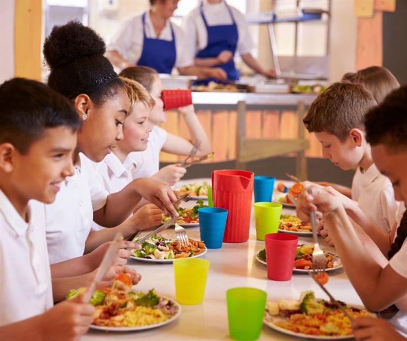 children sit round a table and eat food whilst chatting