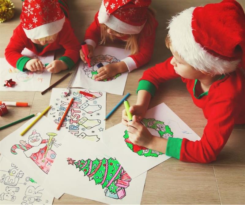 children sit around a table with santa hats on and do drawings and crafts