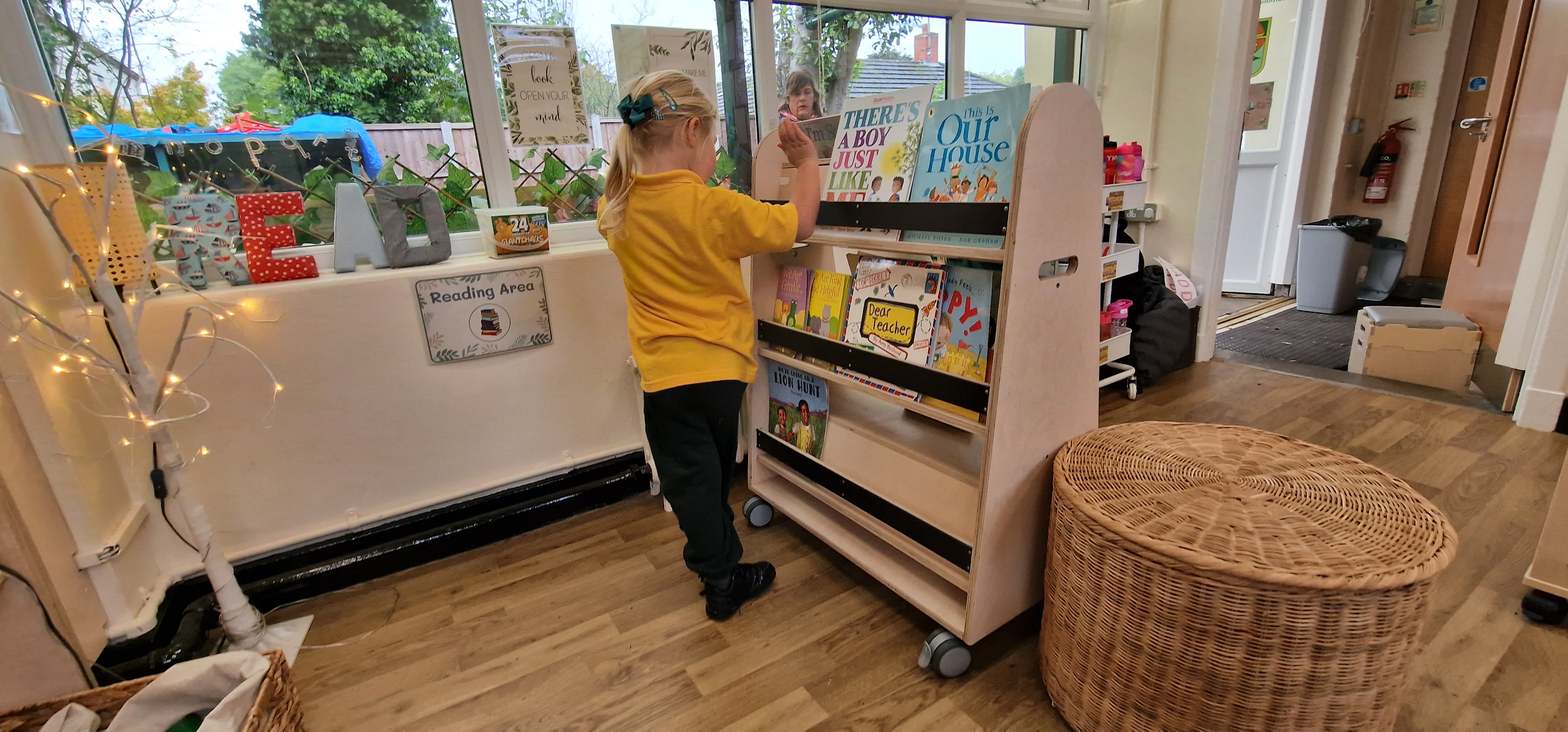 A little girl is going through a bookshelf and is selecting a book to read.