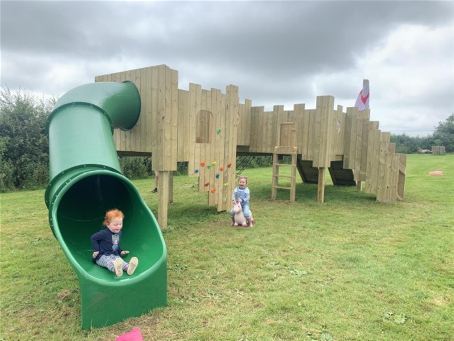A picture of an adventure play park created by Pentagon Play for Chew Moos. The image shows a child happily sliding down a slide, with another child on a toy horse. 