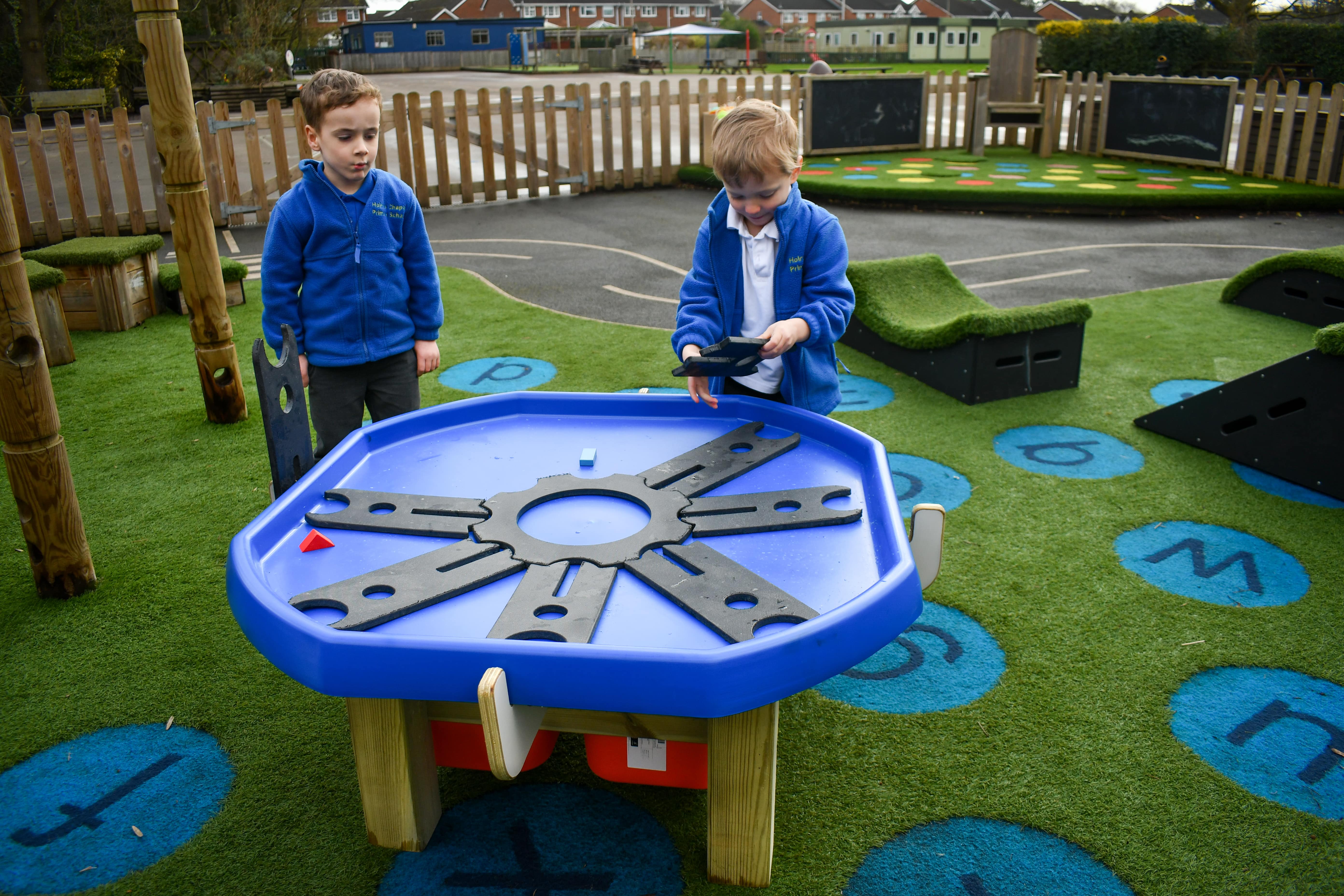 two children are stood around a Tuff table, placing puzzle piece within it. The surrounding area shows some Get Set, Go! Blocks and other playground markings,