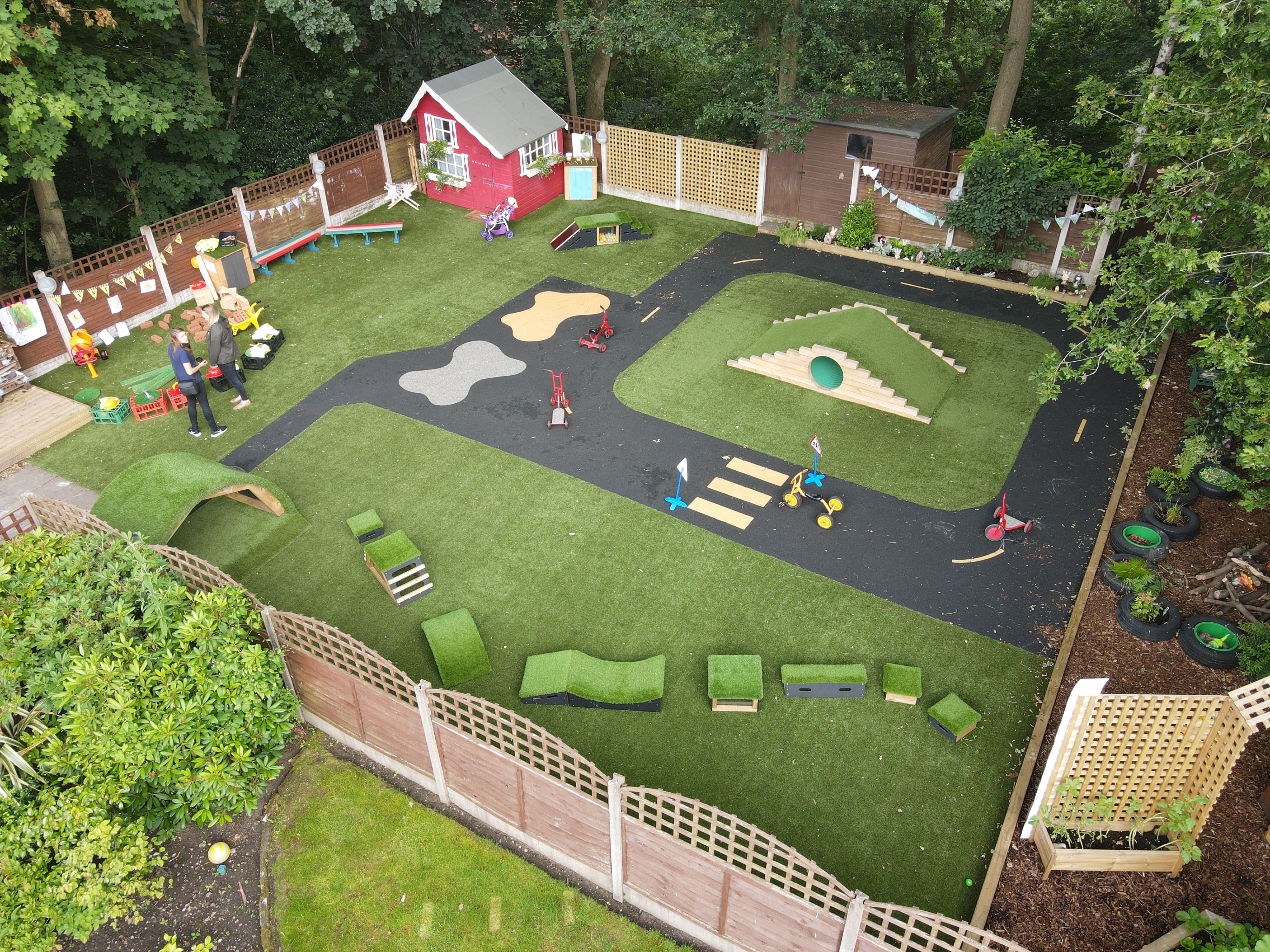 A drone shot showcasing a playground with a wide variety of different playground equipment. A road marking is present, with artificial grass surrounding the whole area.