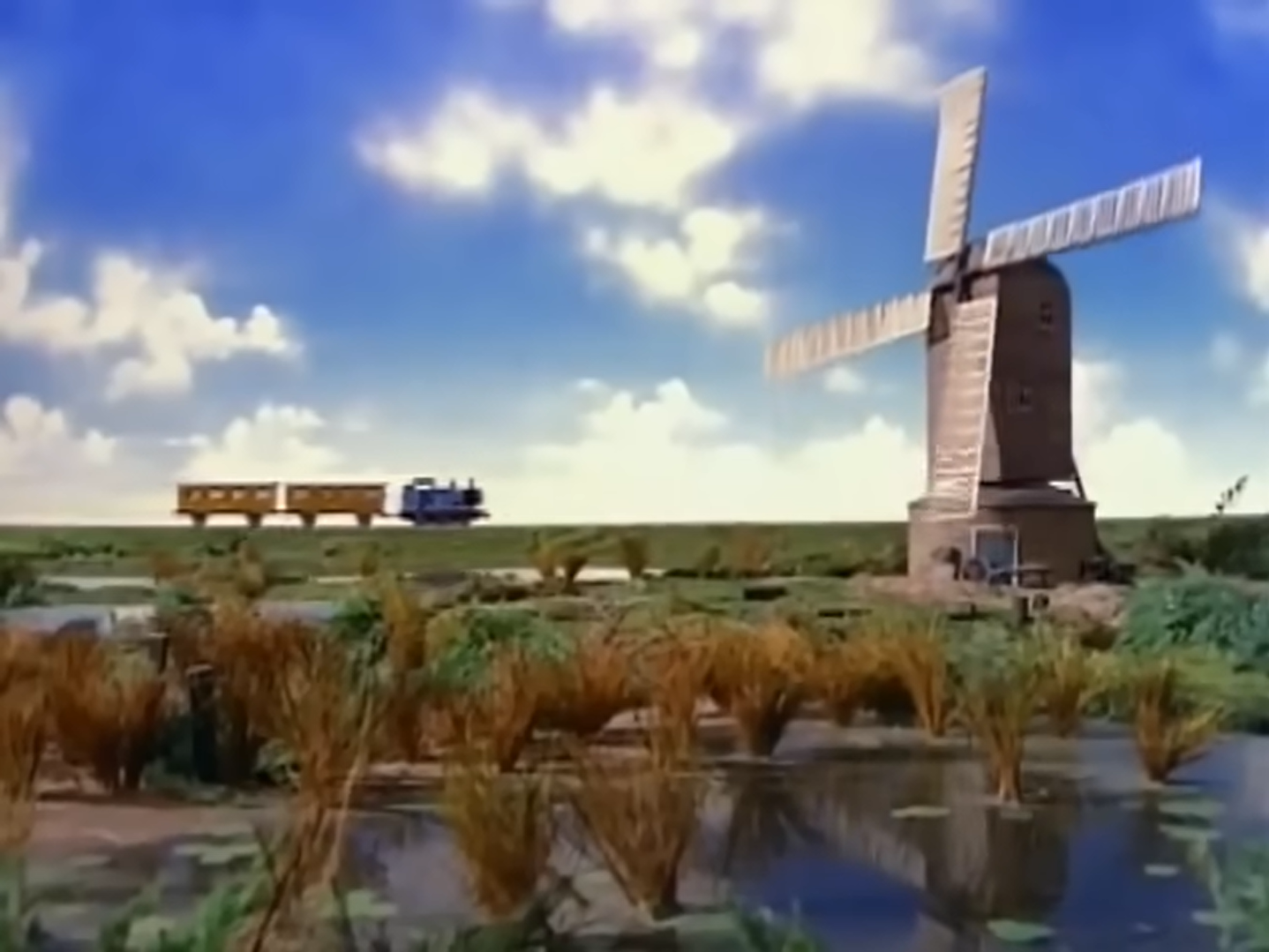 Thomas the tank engine is on a train track which is heading towards a windmill, with a blue sky