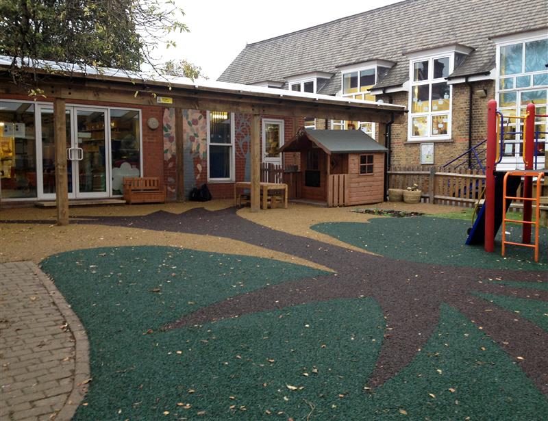 A playbond safety surface for a playground. The design is of a palm tree and is made up of 3 colours, brown, yellow and green. There is a play tower to the right and a concrete flagged path to the left.