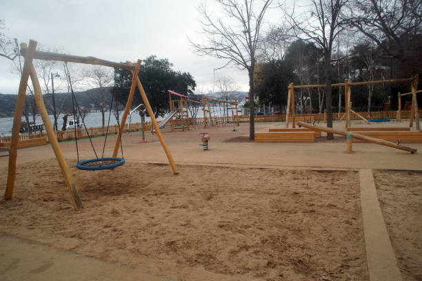 A variety of different play equipment on a playground, with sand being used as the safety surface. Concrete is in-between the sand, separating the play equipment. 