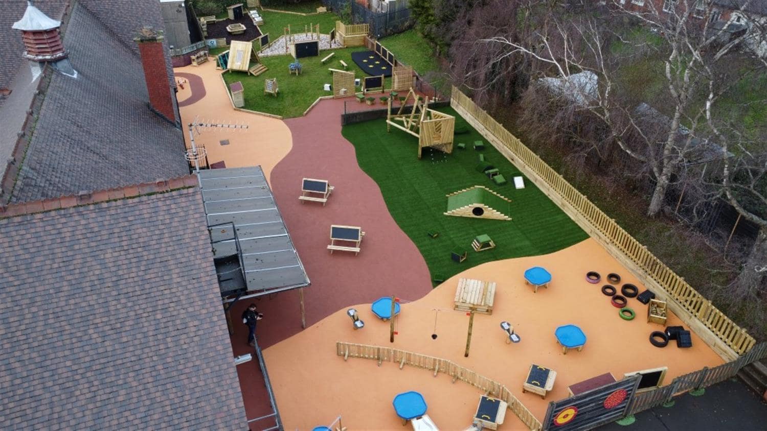 A huge playground that has a mixture of wetpour and artificial grass surfacing. The wetpour is red and orange and has a variety of play equipment placed on top of it. The artificial grass has bigger play equipment installed on it.