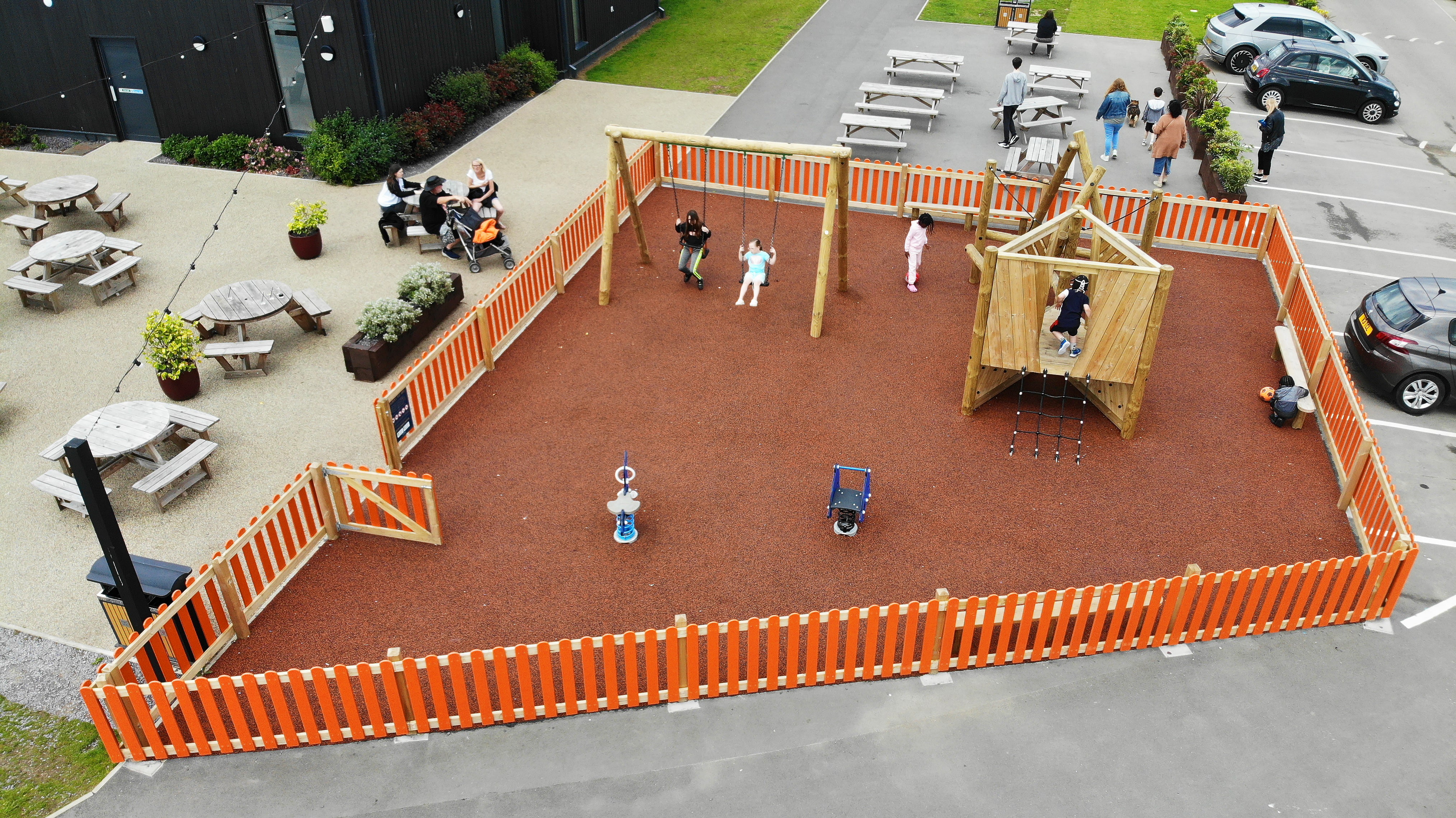 An orange wetpour playground with a Harter Fell climbing frame, a timber swing, two springs and a perch bench.