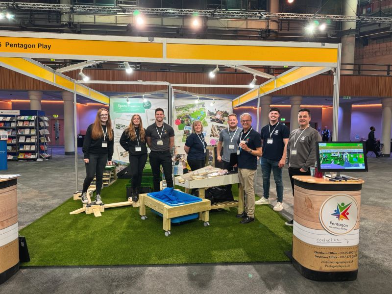 A group of Pentagon Play employees attending a conference. They are stood underneath a Pentagon Play stall.