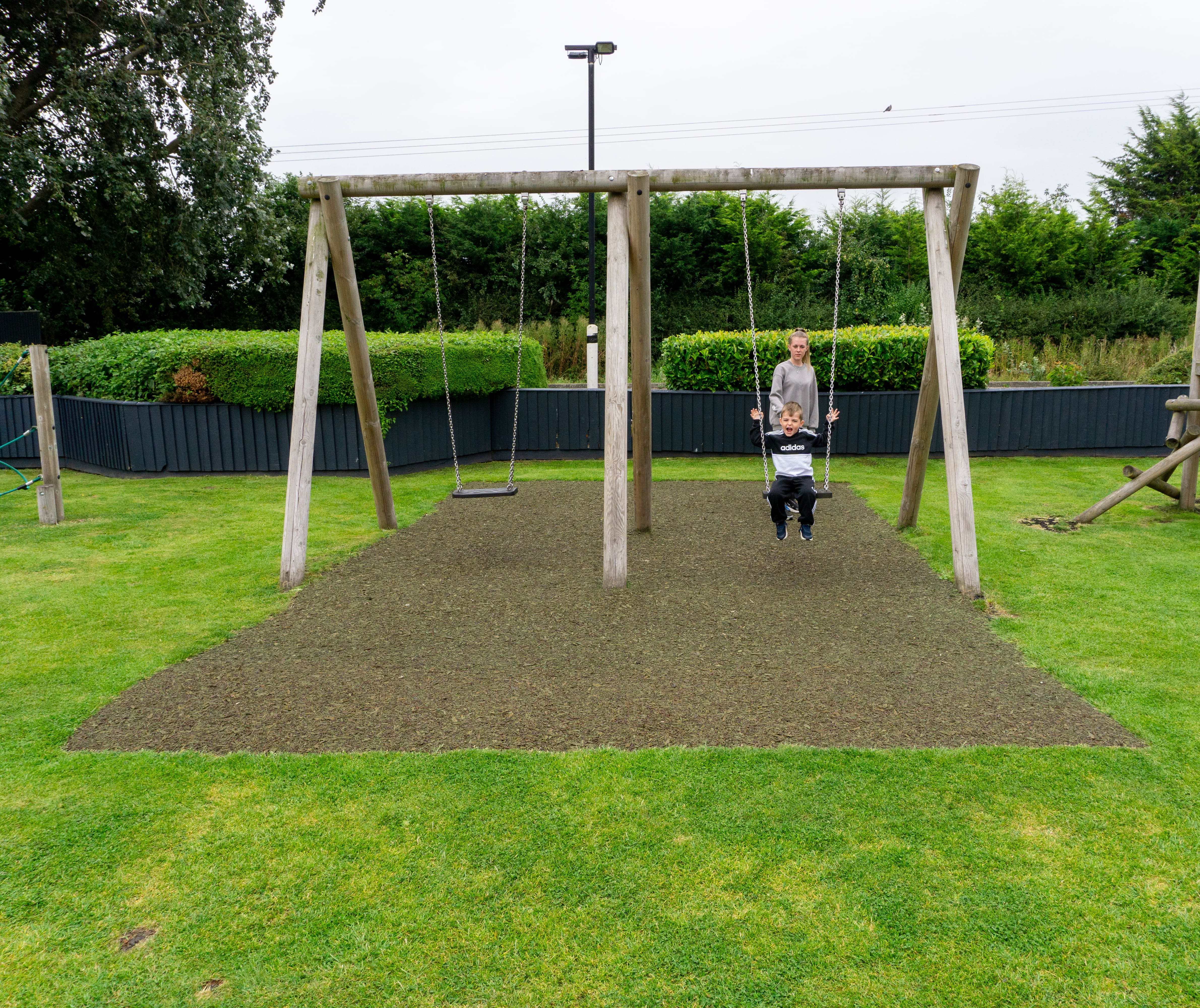 A Playbond surface that has been installed underneath a set of swings. Two children are using the swings.