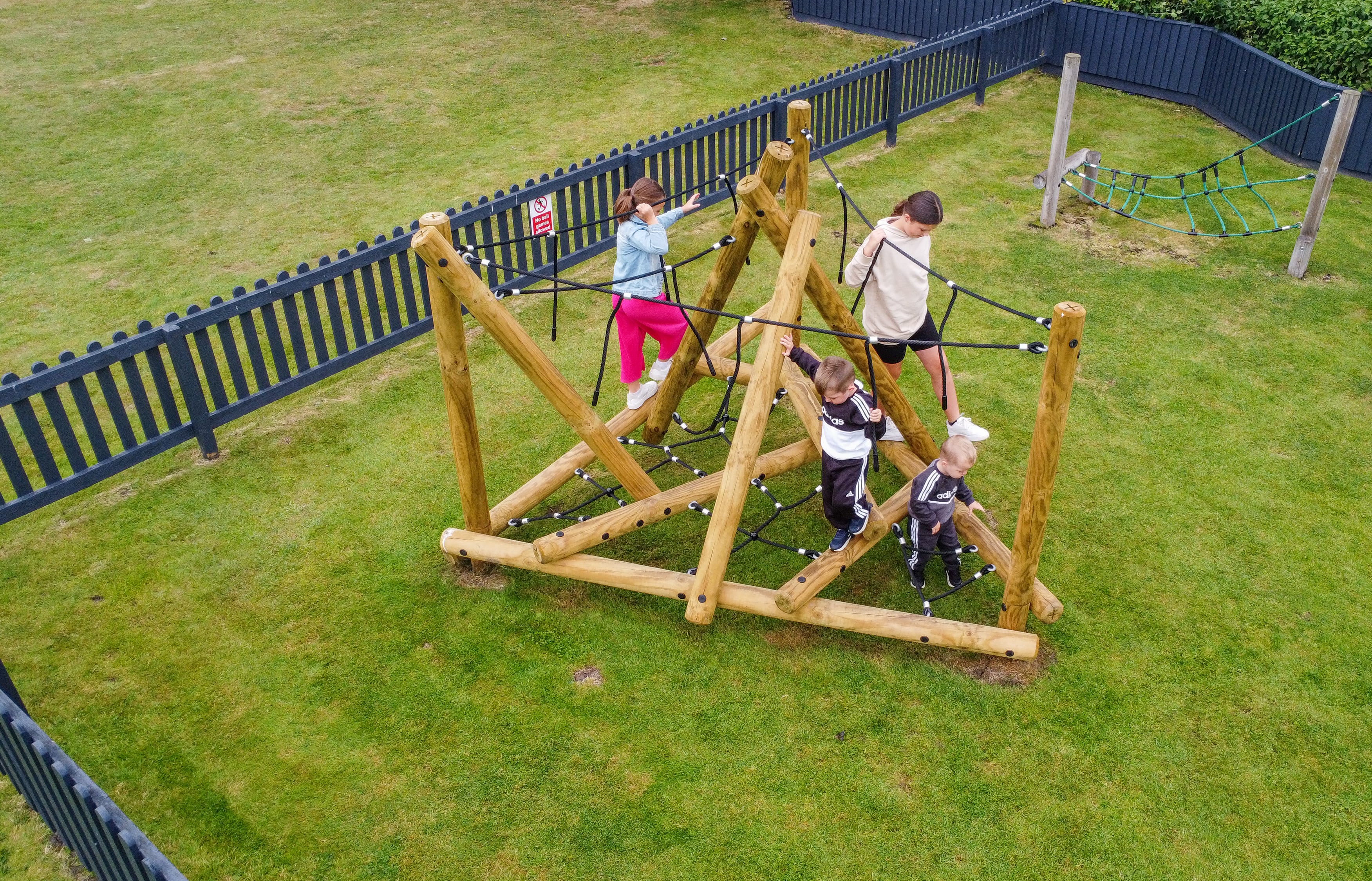 A drone shot of the Mam Tor Mountain Climber, showing a group of children playing on the piece of play equipment. A black wooden fence can be seen around the play equipment.