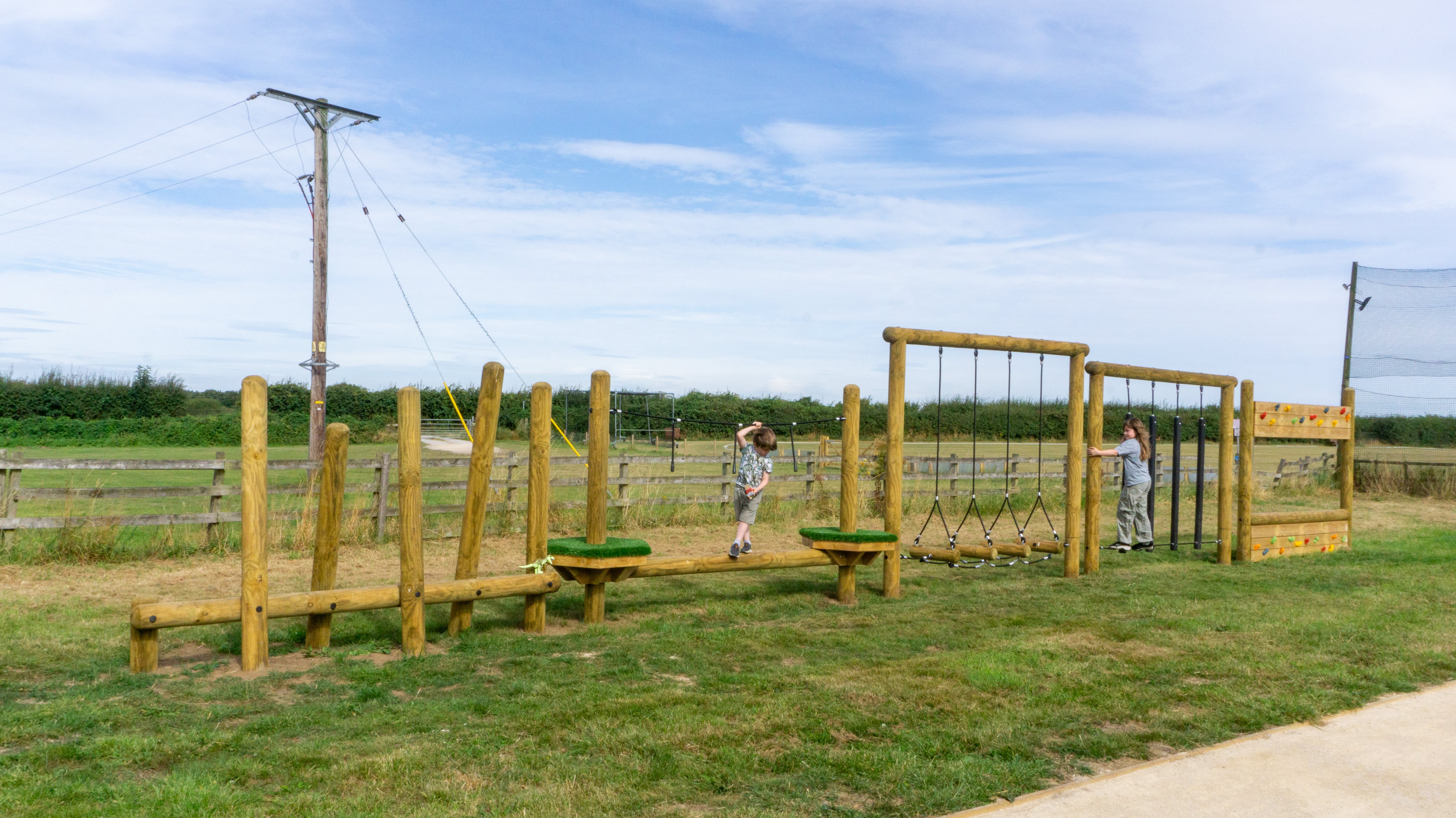 A wide range shot showing two children exploring the full Trim Trail. The wooden Trim Trail has been installed on natural turf.