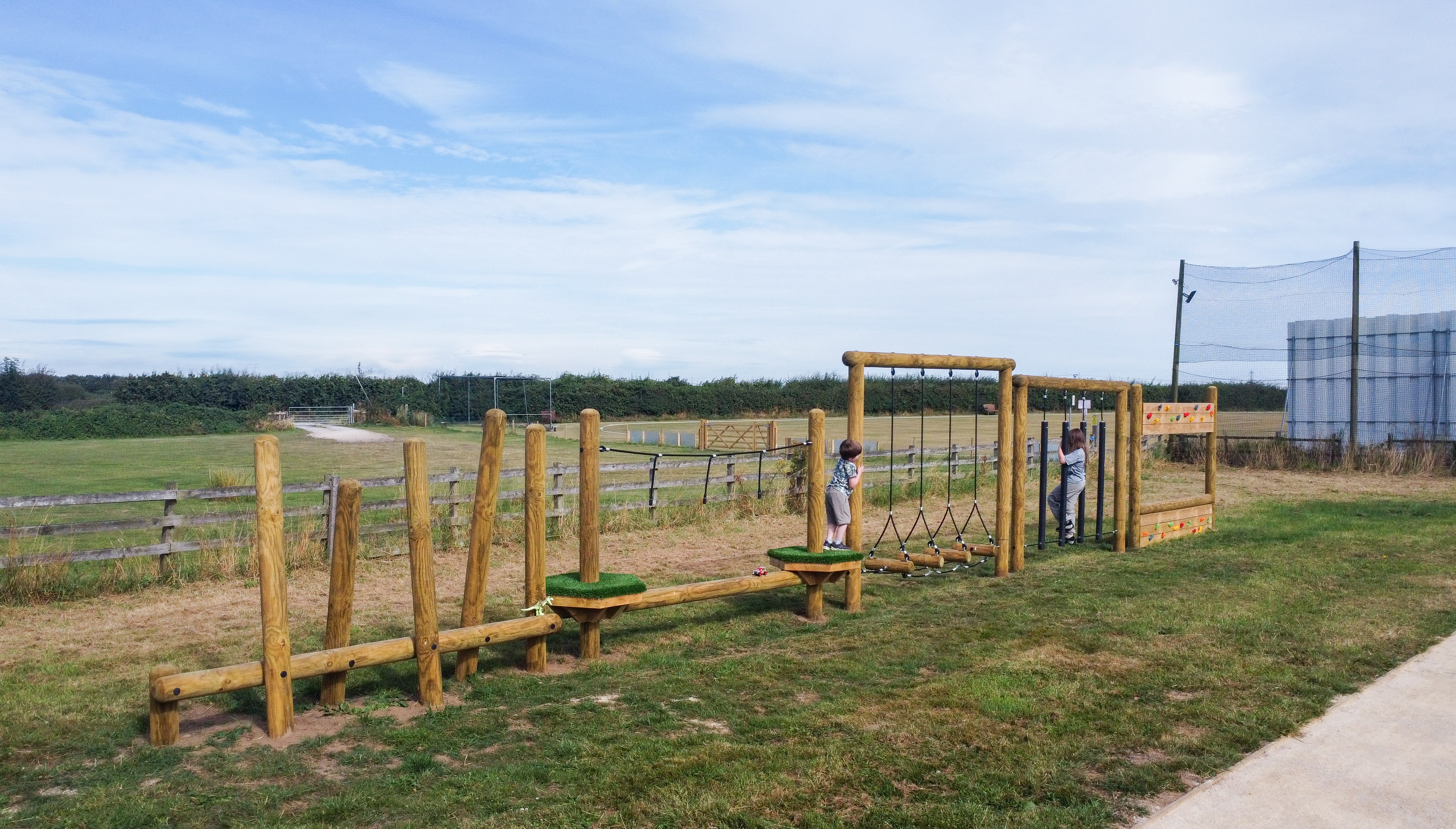 A photo which showcases the full size of the bespoke Trim Trail that we installed at Hensall Community Garden. Two children are making their way through the challenges.