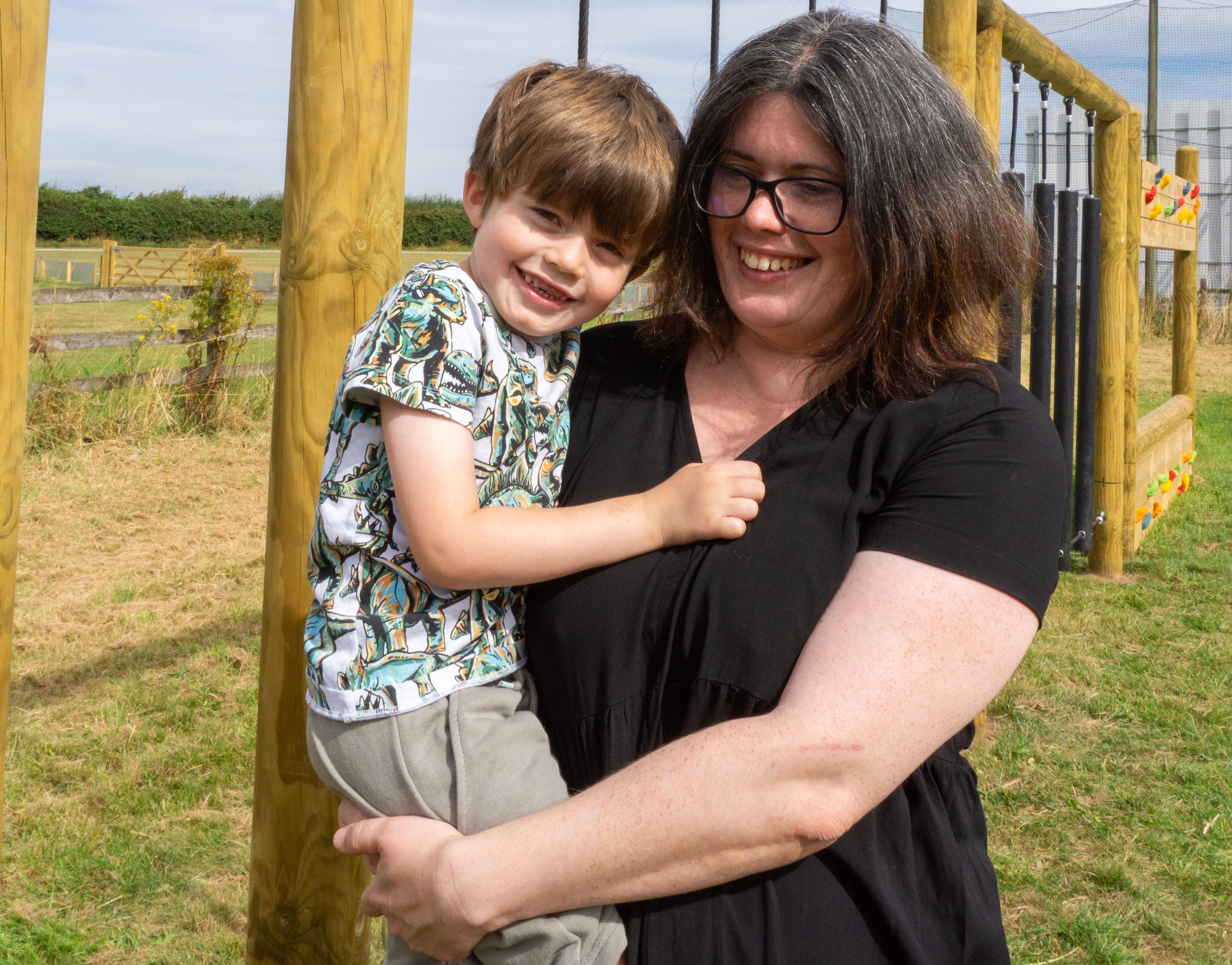 A picture showing a woman with medium length, dark brown hair called Imogen Bellaby. The woman is holding her son up as he looks into the camera.