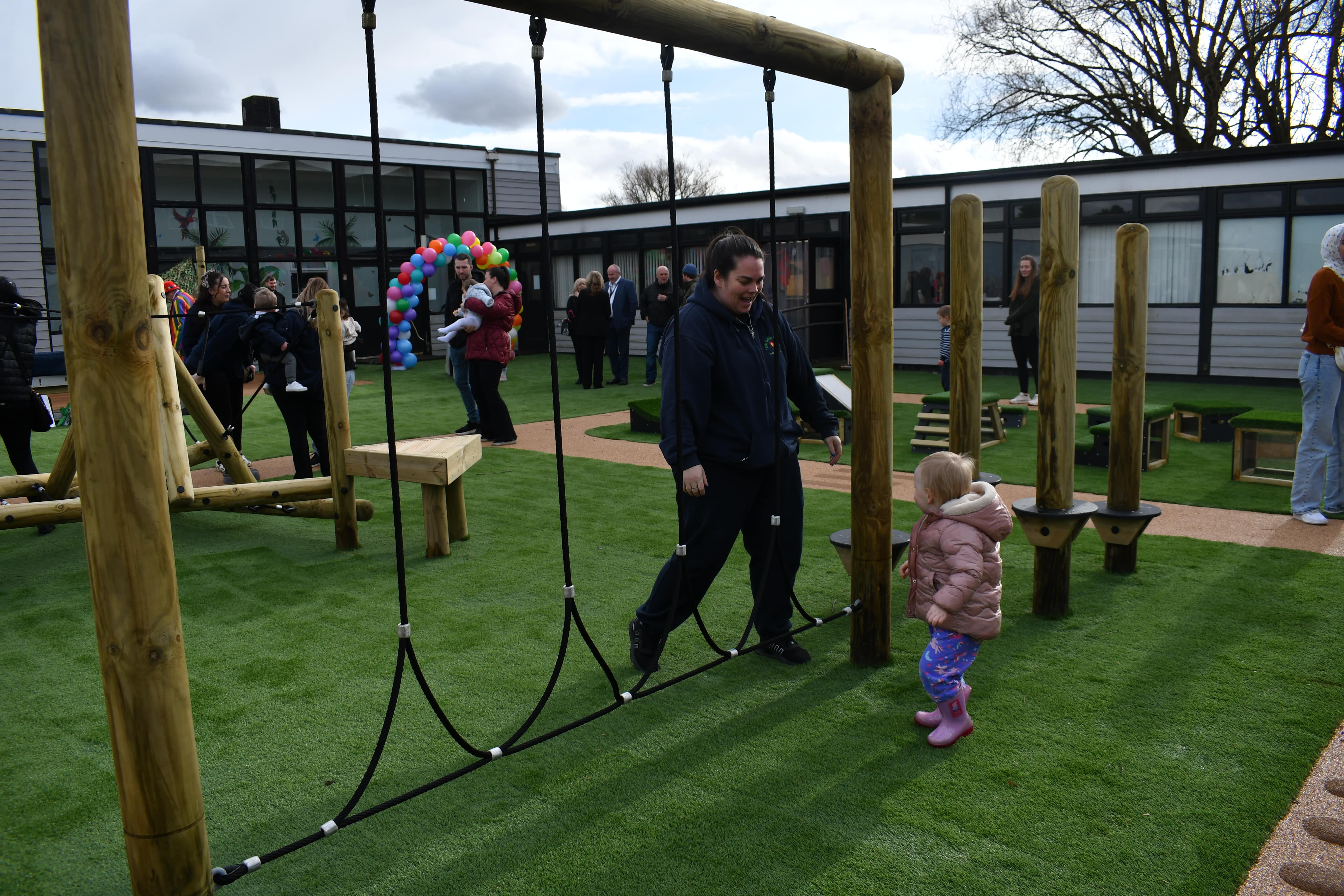 A group of children and adults are exploring the new play area, with a variety of commercial outdoor play equipment being seen in the shot.