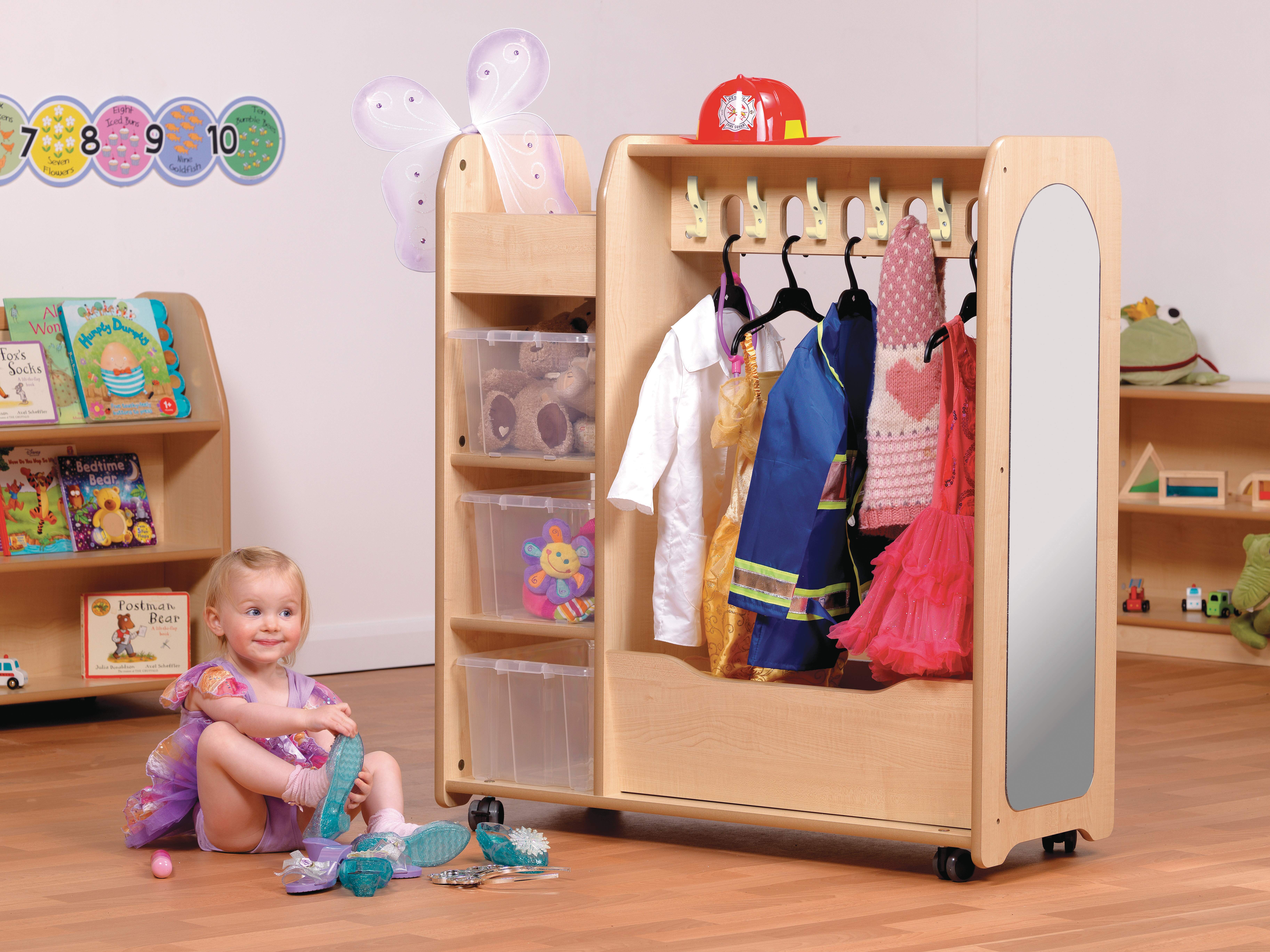 A little girl is sat on the floor as she is putting a shoe on her foot. Next to her is a Role Play cupboard, full of different imaginative costumes and props.