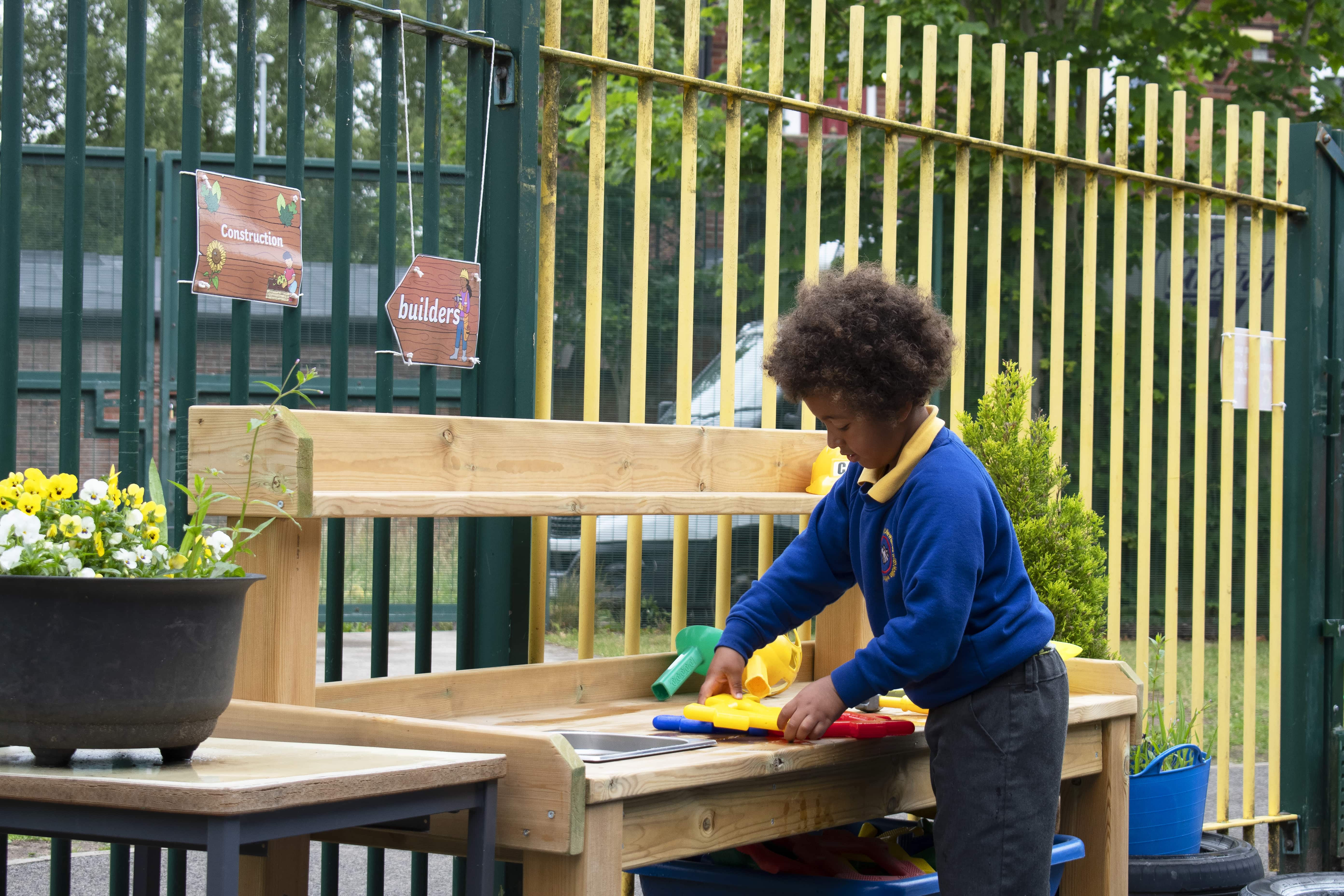 A child is performing an activity on a wooden planter table as they move objects around