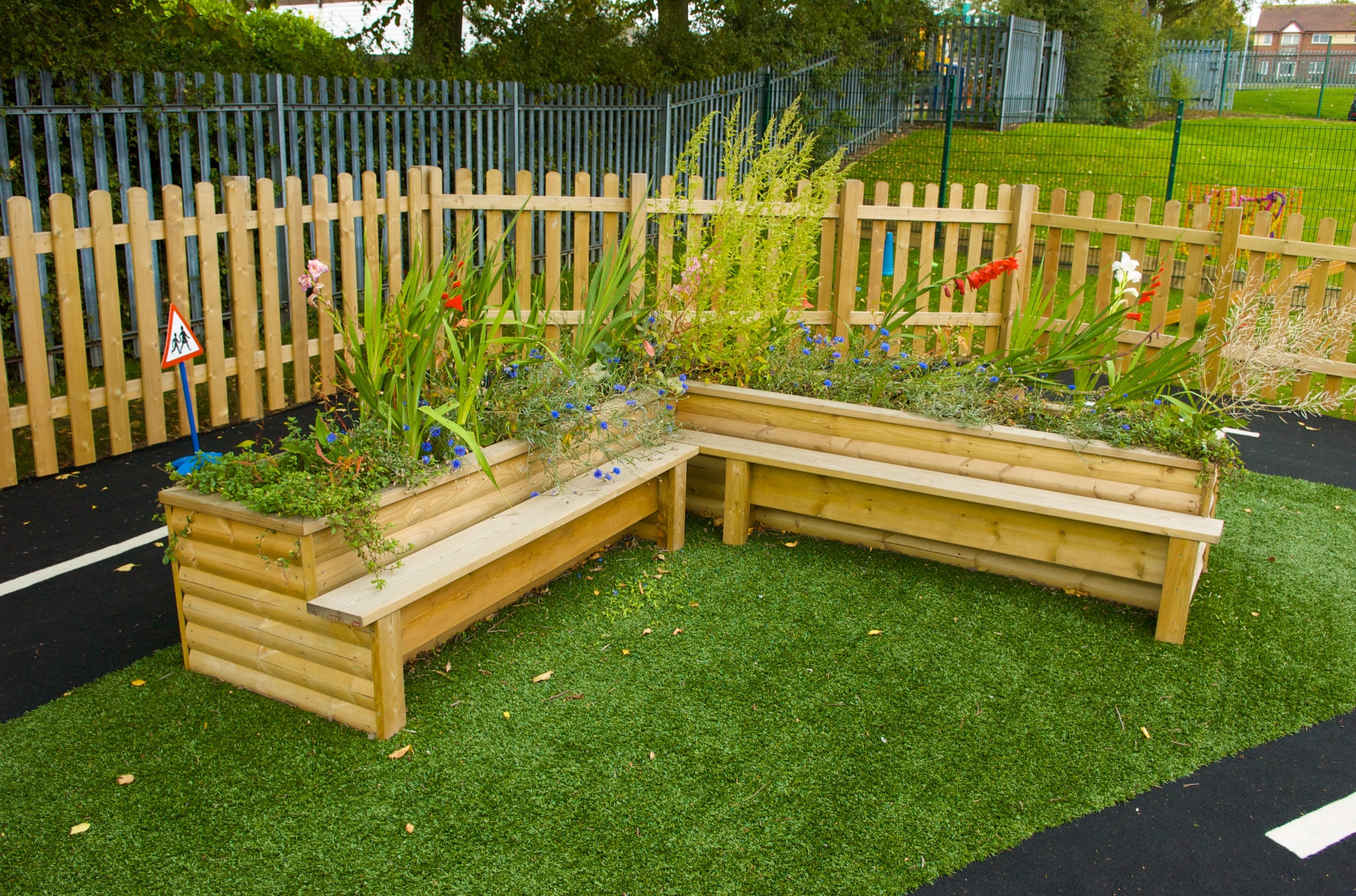 A planter that has been built at a 90 degree angle. It offers seating built into the planter. There are plants growing from the planters.