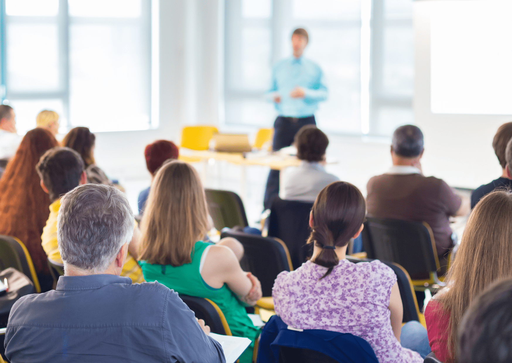 A group of teachers are sat in a room looking at a man who is doing a presentation.