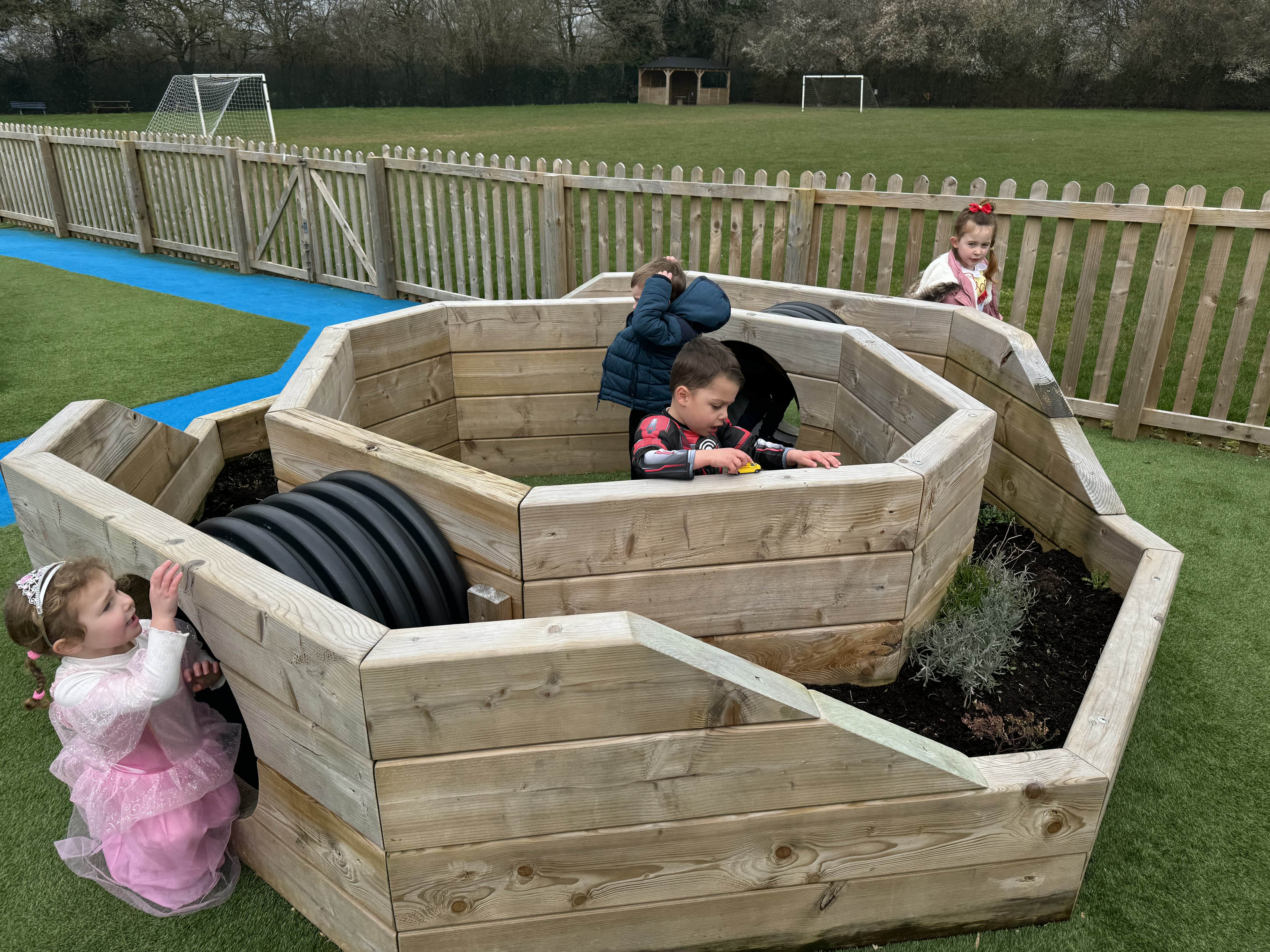 A high angle shot that shows the immersive planter. Two children can be seen getting ready to climb through the tunnels that lead to the centre of the planter. A child is already at the centre and is playing with a toy car.