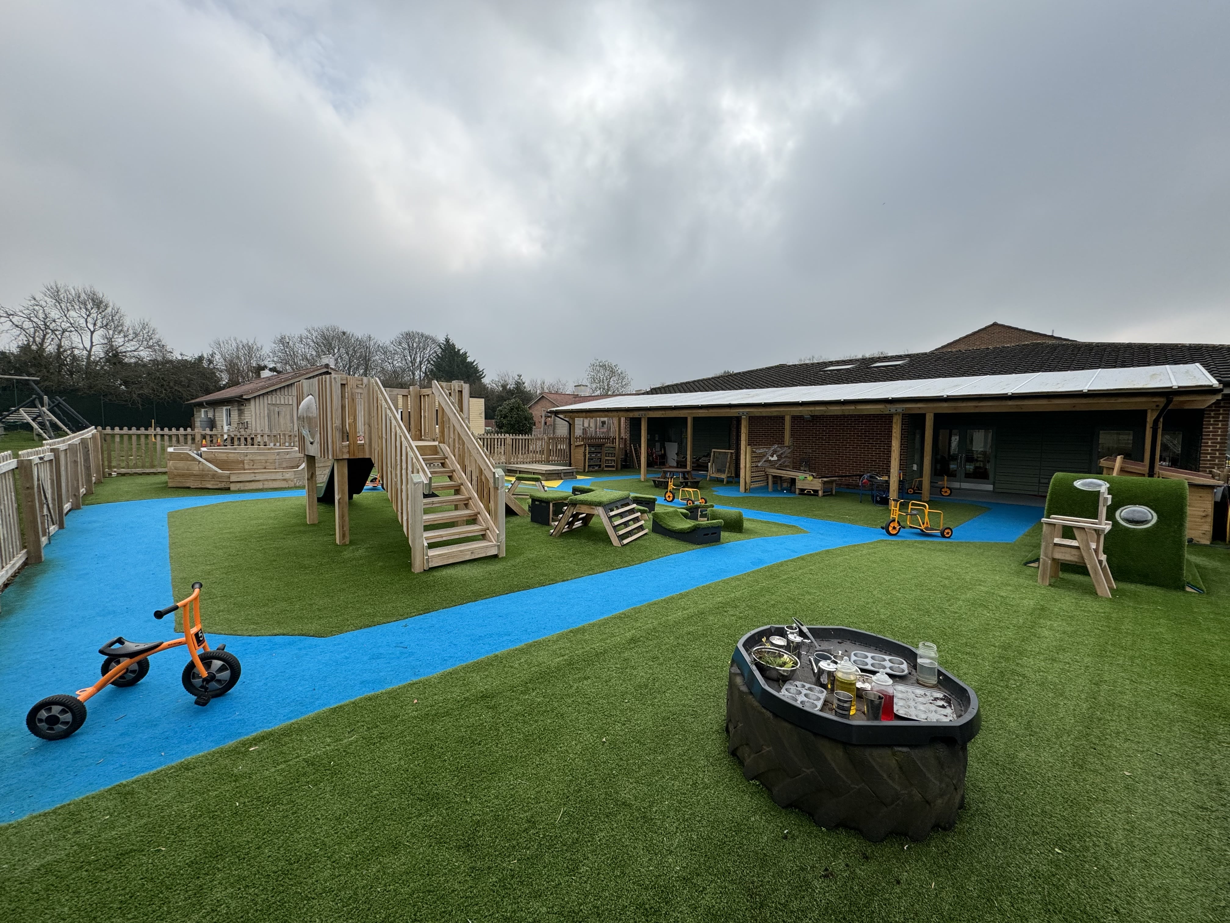 Play equipment that has been installed in the centre of an artificial grass playground. The grass is green with a blue pathway design going around the main bulk of play equipment.