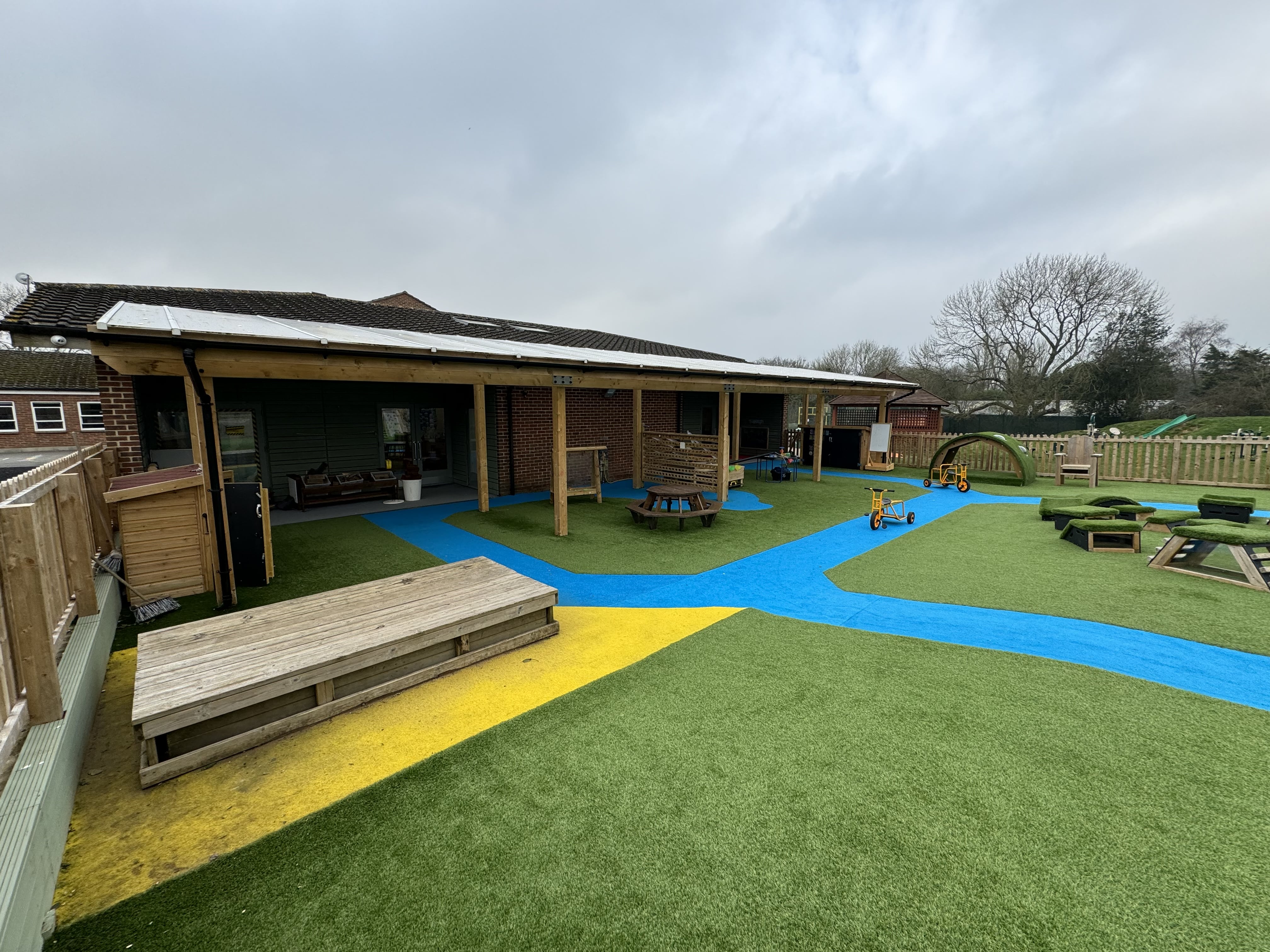 A landscape photo showcasing the artificial grass surfacing for a playground. The grass is in three different colours, green, blue and yellow.