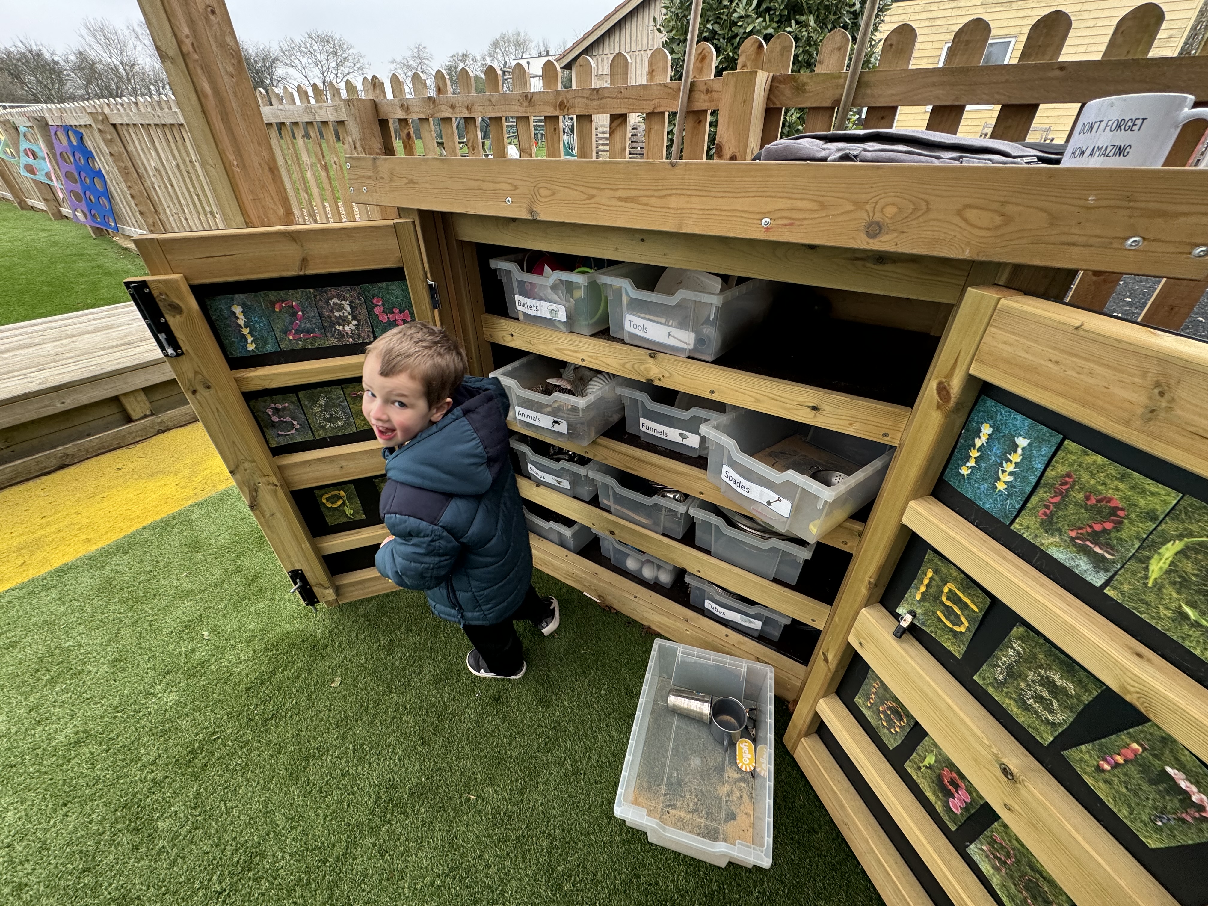 A child has opened the storage unit and is exploring all of the different sections. The child is looking at the camera and smiling, with letter stickters stuck on the inside of the doors.