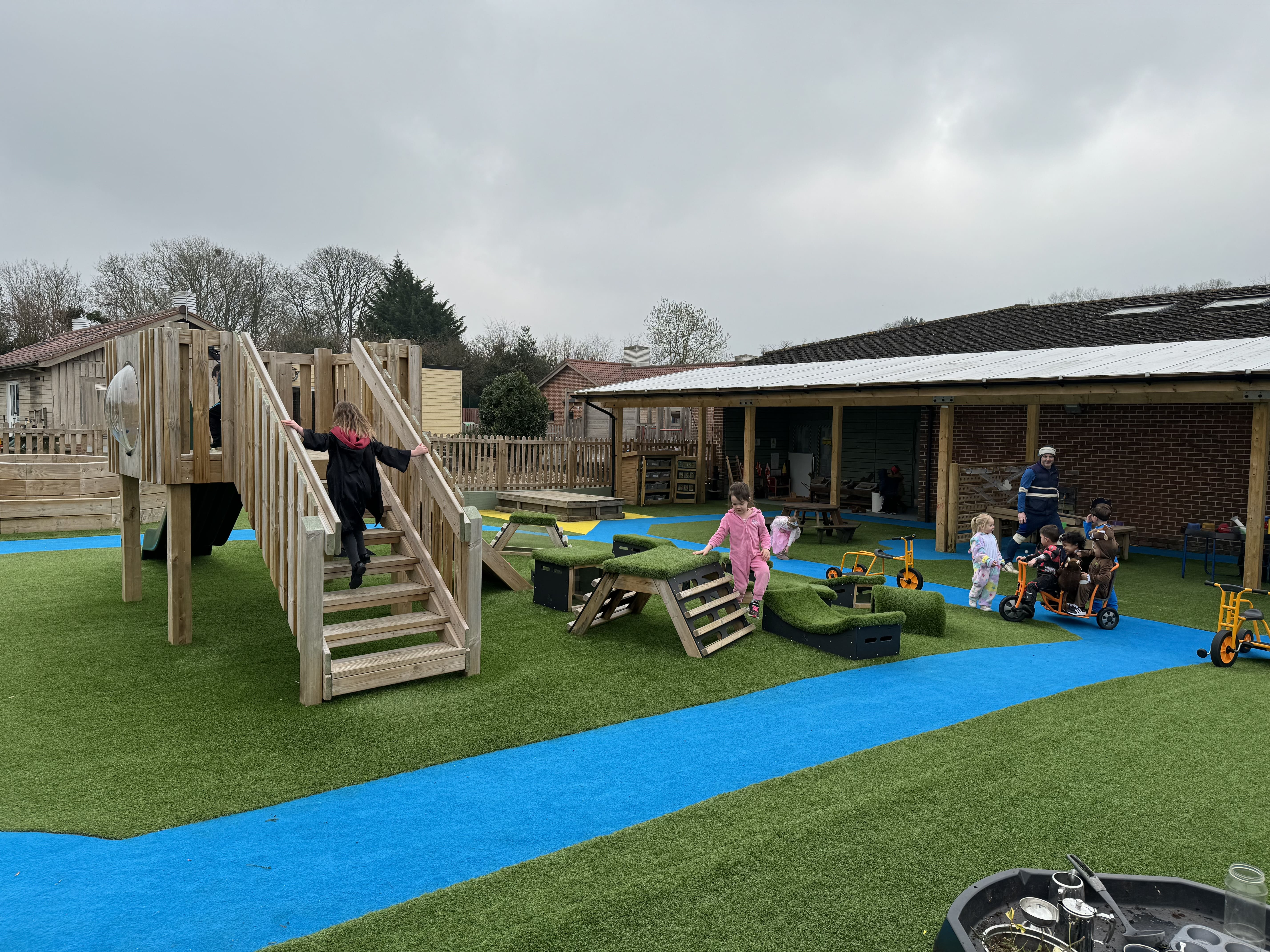 A play tower can be seen with a group of children playing with it and surrounding equipment. The children are smiling and cheering as they explore.