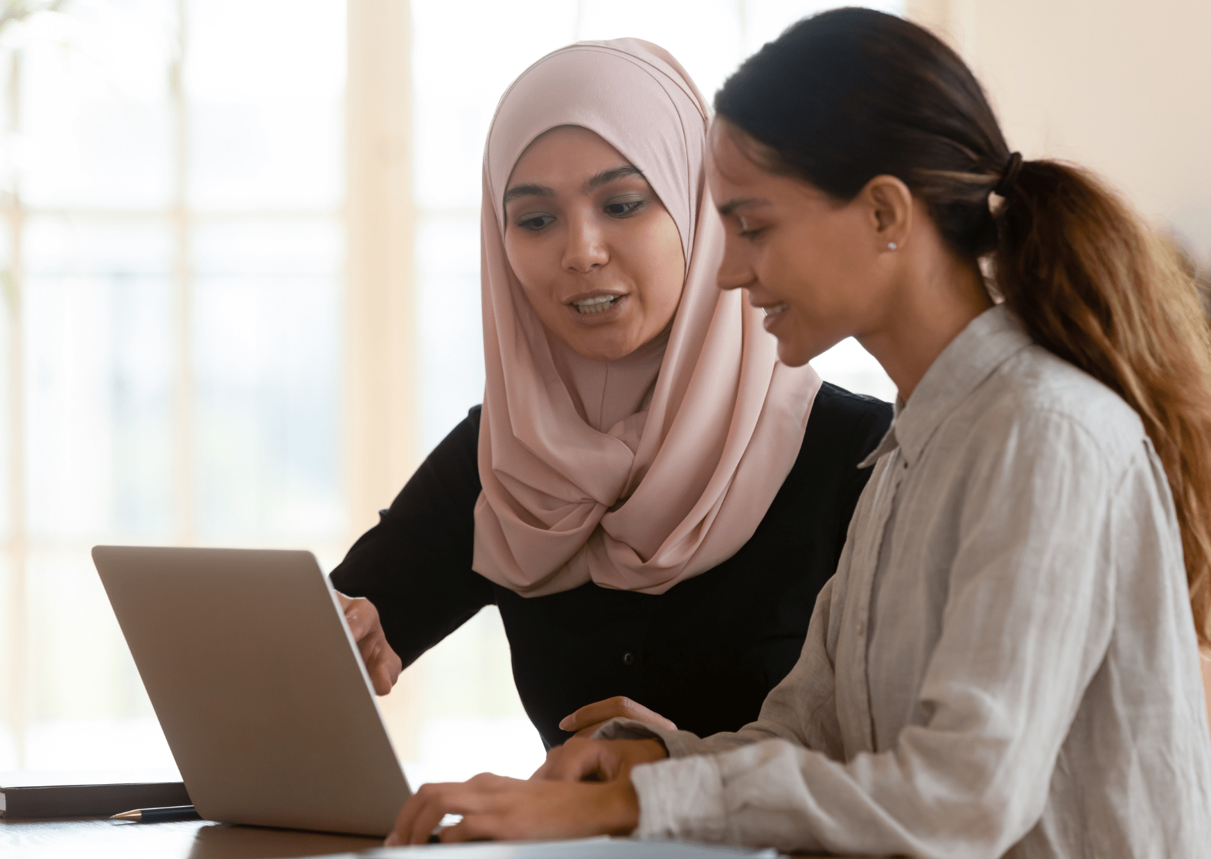 A teaching assistant and a young woman are sat at a table with a laptop open. They are looking through the process of applying for a blue card.