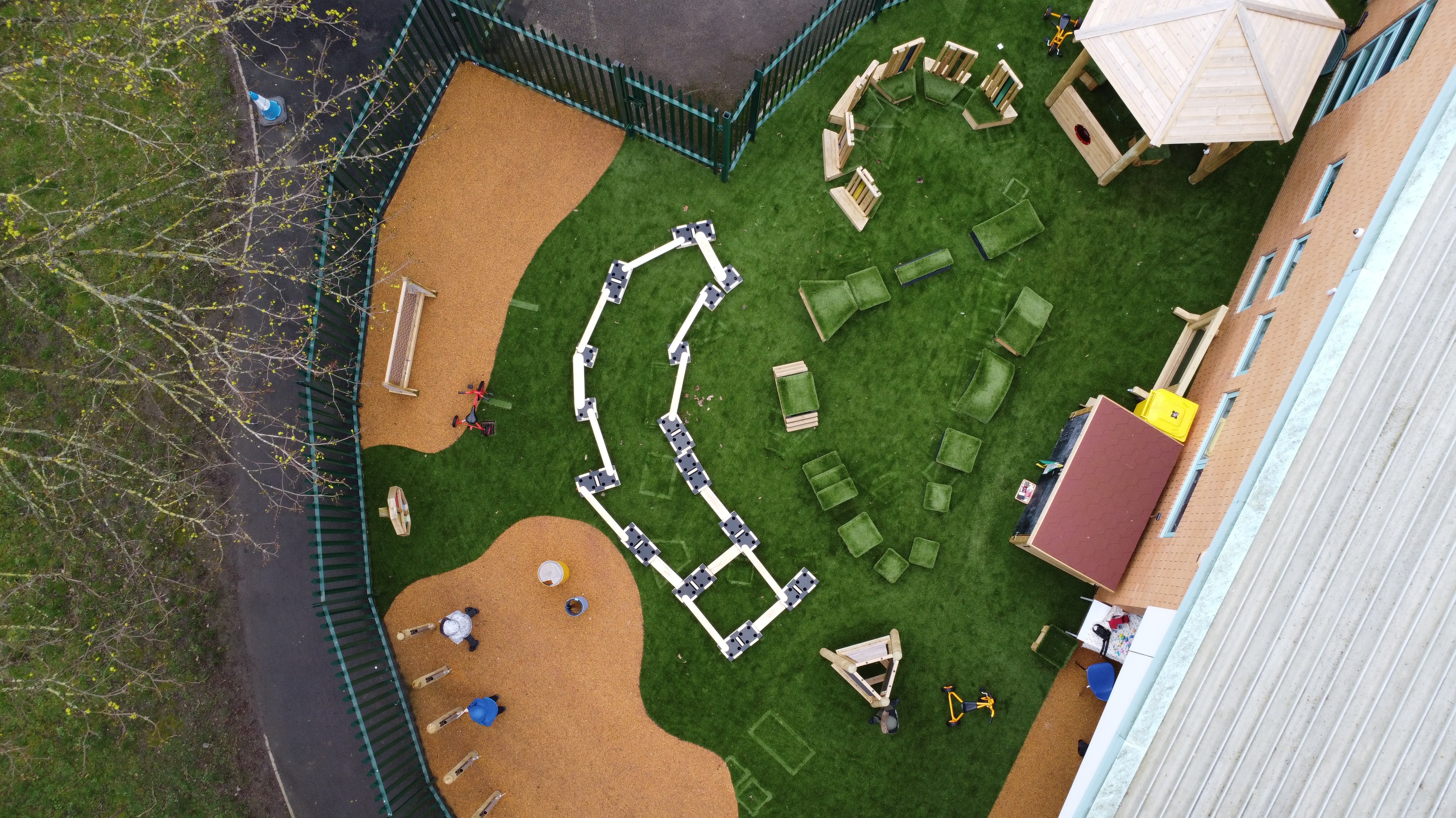 Artificial grass and wetpour have been installed together at a playground. The artificial grass is green and the wetpour is orange, creating a contrasting scheme. A variety of play equipment has been placed on the area.