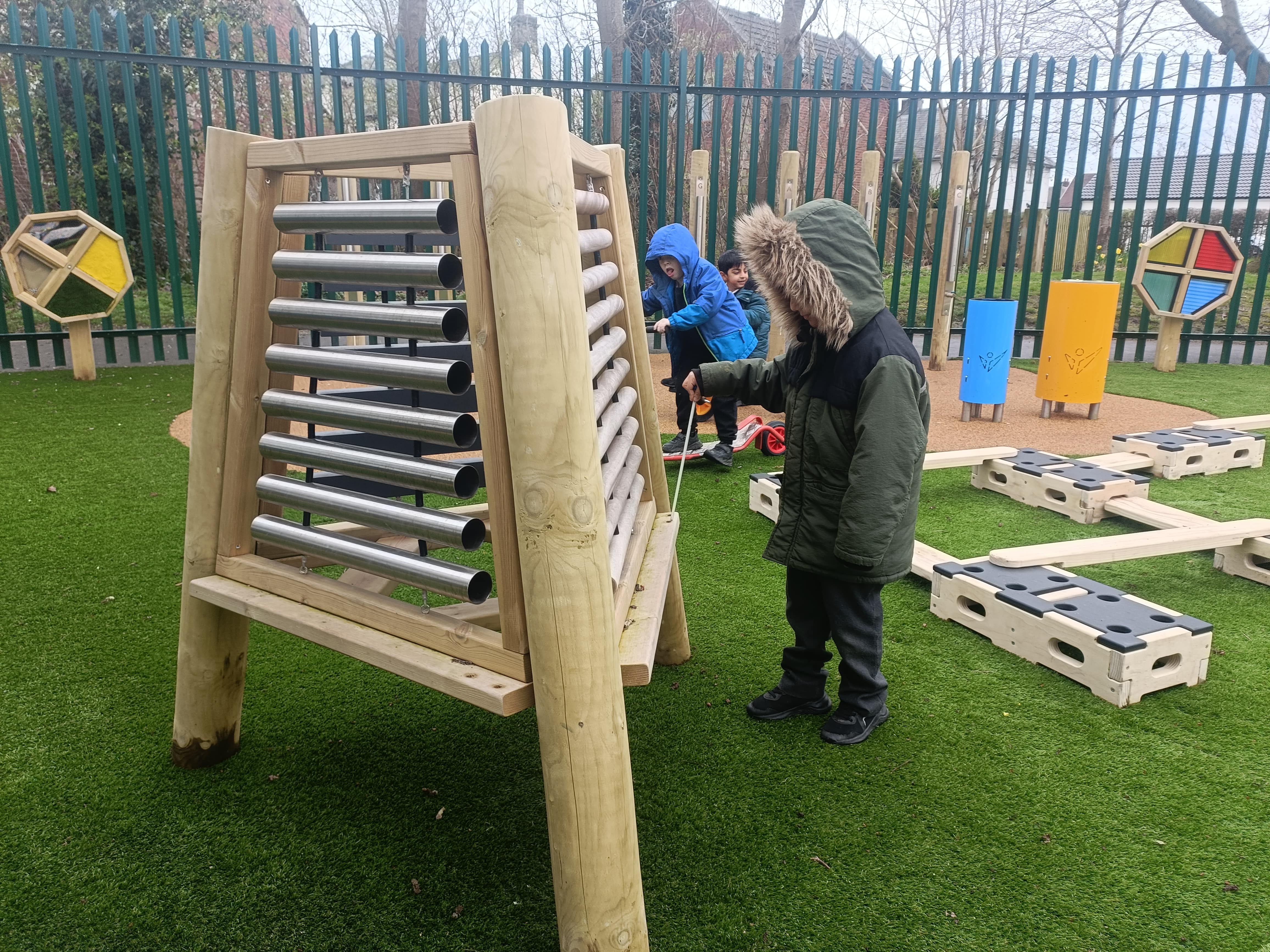 A child is playing with a freestanding piece of music equipment, which has been placed on artificial grass. Other pieces of play equipment can be seen in the background.