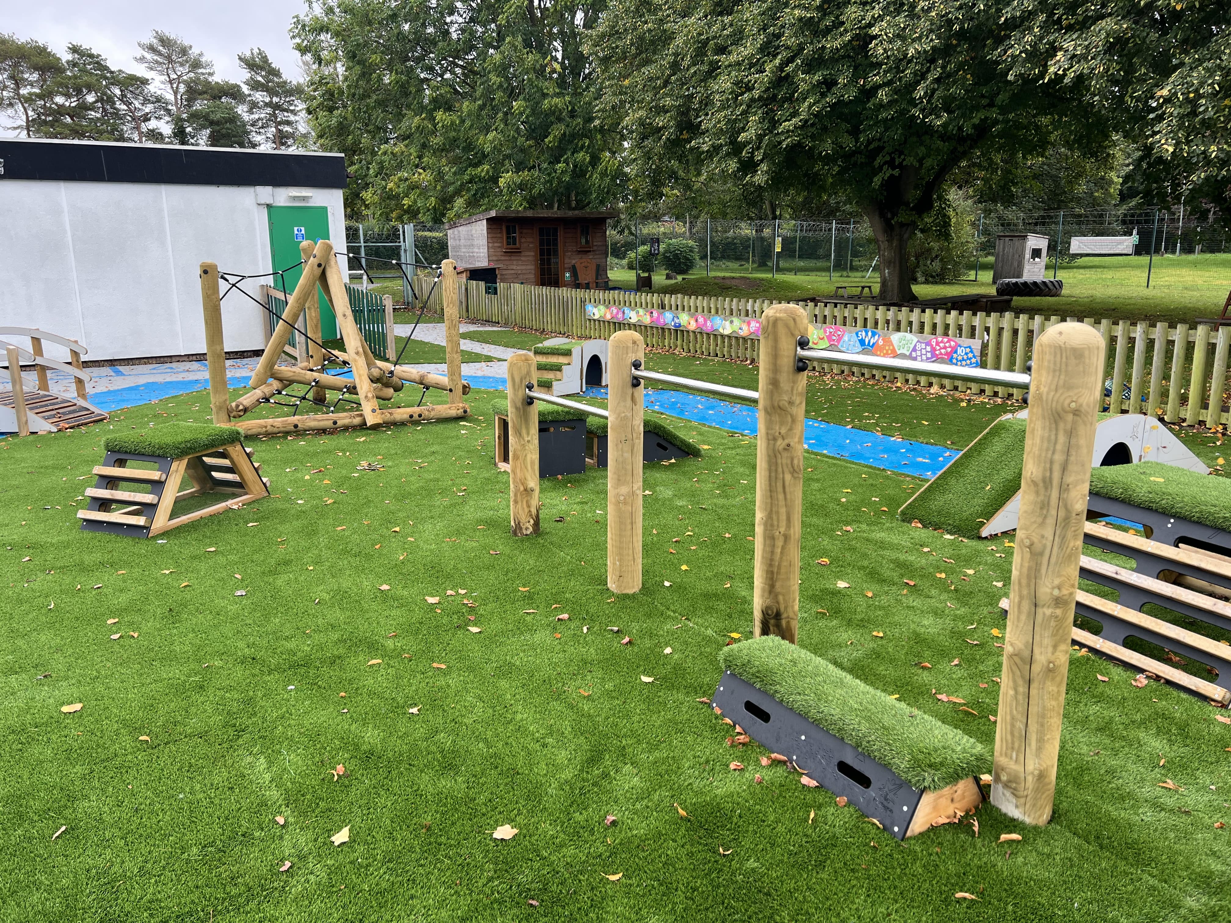 An active play area that has been installed on artificial grass and contains a variety of outdoor gym equipment.