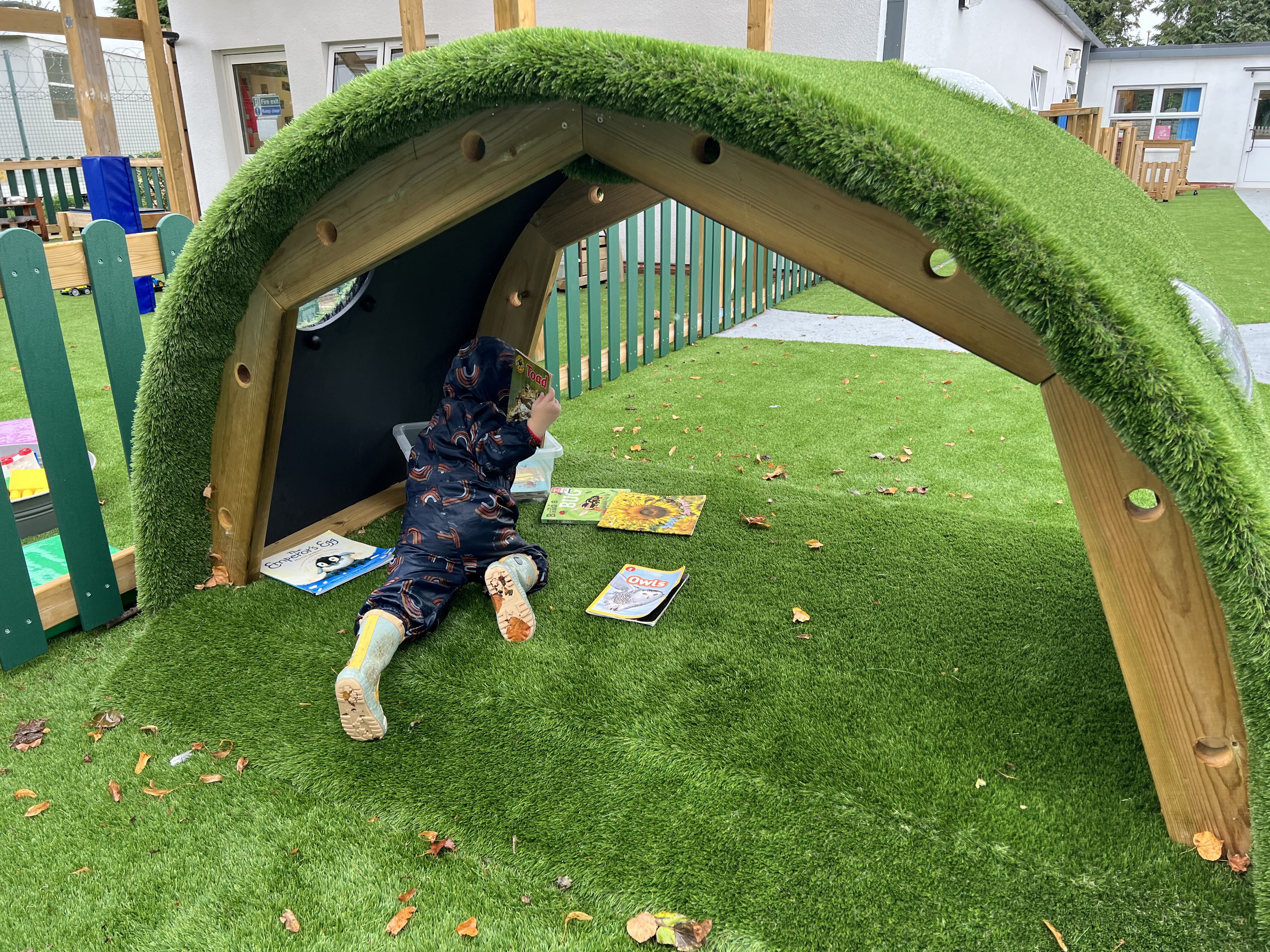 A little child is lay beneath the Hill Den as they are reading a book, engaging in independent play.